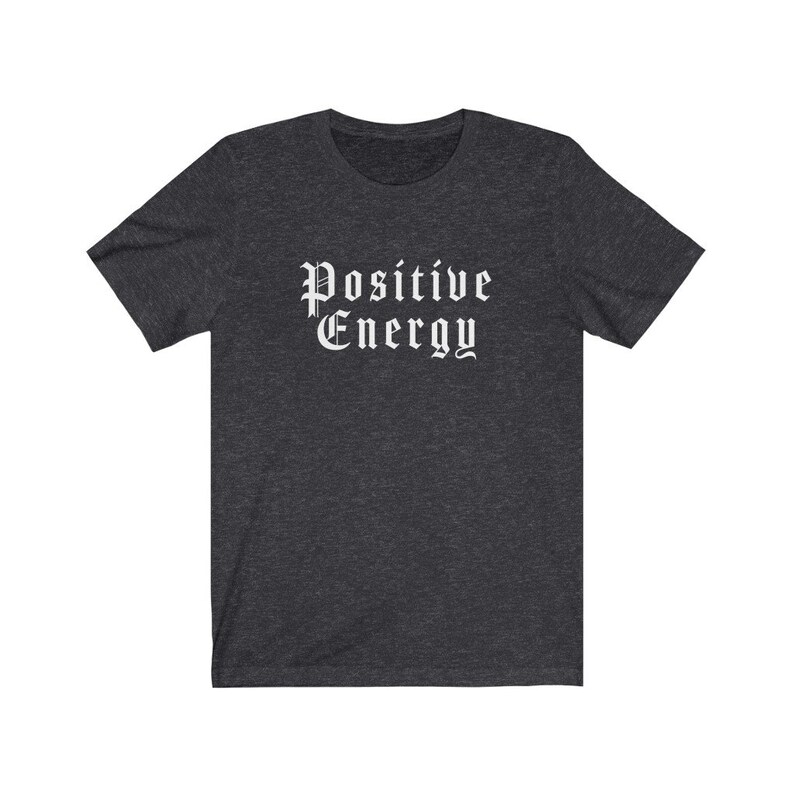 May include: Dark gray t-shirt with the words "Positive Energy" in a white gothic font. The shirt has short sleeves and a crew neck. The fabric appears to be a soft, heathered material.
