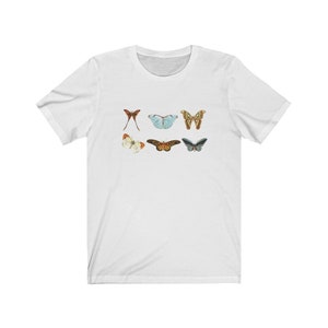 May include: White t-shirt featuring six colorful butterfly illustrations. The butterflies are in various colors, including red, blue, brown, and green. The shirt is made of a soft material and has a classic crew neck.