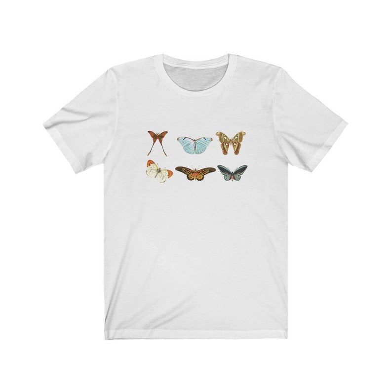 May include: White t-shirt featuring six colorful butterfly illustrations. The butterflies are in various colors, including red, blue, brown, and green. The shirt is made of a soft material and has a classic crew neck.
