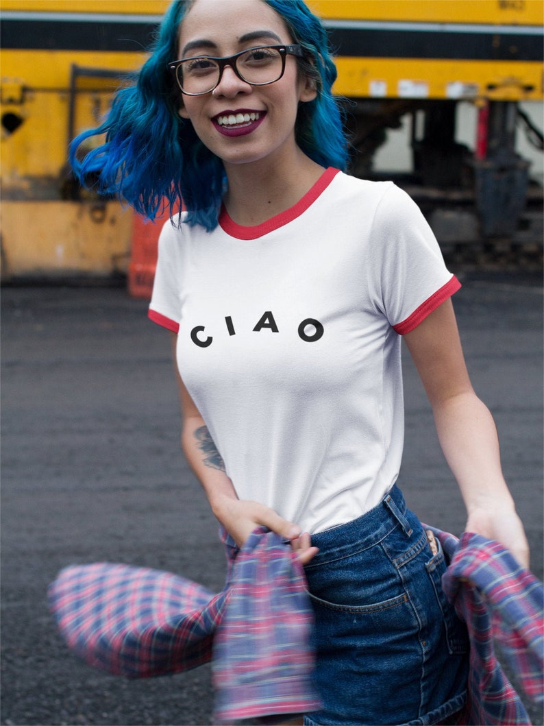 May include: White t-shirt with red trim and the word "CIAO" in black letters. The person is wearing blue denim shorts and a red and blue plaid shirt. The person is also wearing black glasses.