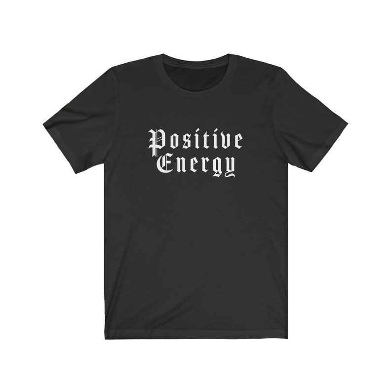 May include: A black t-shirt with the words "Positive Energy" printed in a gothic font. The text is in white and centered on the front of the shirt. The shirt has short sleeves and a crew neck.