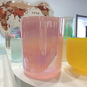 Könnte beinhalten: Eine Sammlung von irisierenden Glas-Kerzenhaltern in verschiedenen Farben. Der Hauptkerzenhalter hat eine große, zylindrische Form mit einem rosa-pfirsichfarbenen Farbverlauf. Weitere Halter sind in Grün- und Gelbtönen zu sehen.
