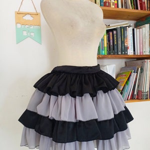 Puede incluir: Una falda negra y gris de capas con volantes. La falda est&aacute; en un maniqu&iacute; blanco.
