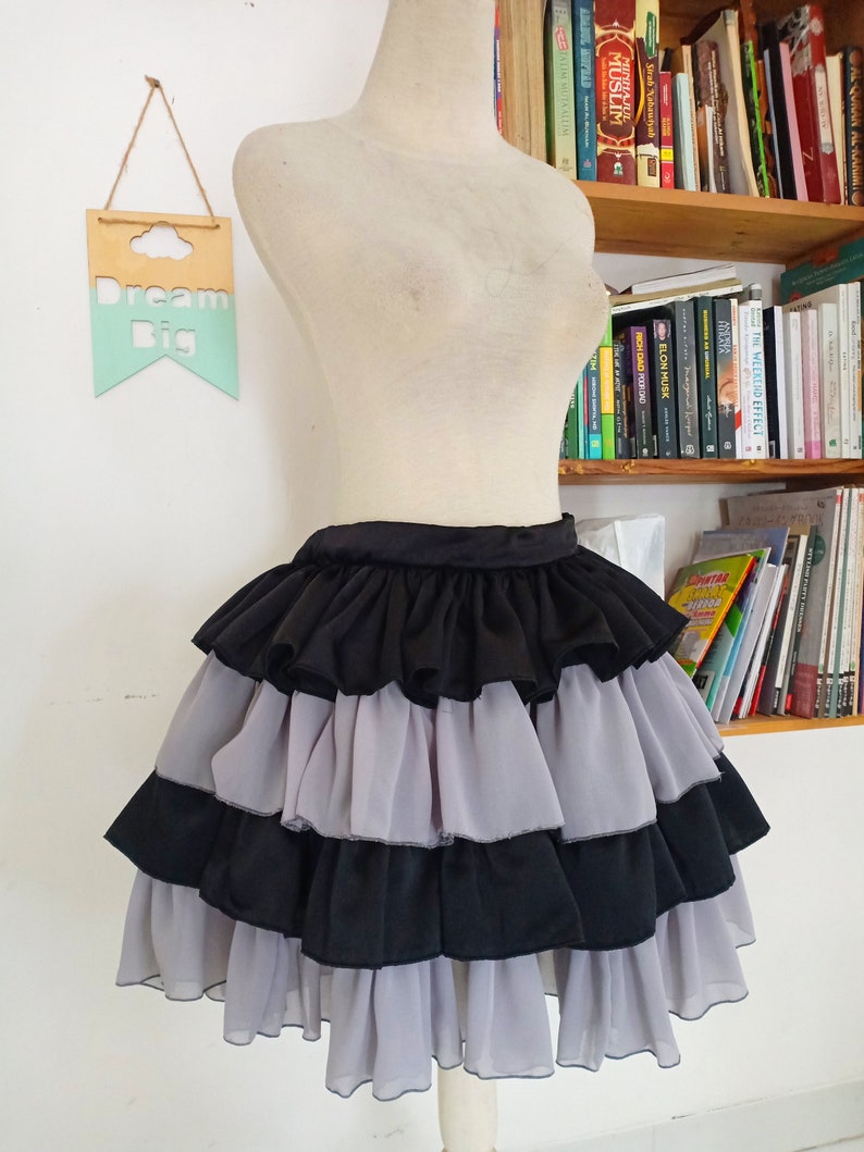 Puede incluir: Una falda negra y gris de capas con volantes. La falda est&aacute; en un maniqu&iacute; blanco.