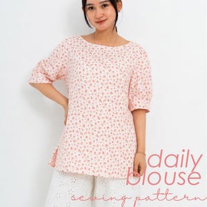 Może przedstawiać: Jasnoróżowa bluzka w drobny czerwony kwiatowy wzór, z dekoltem w łódkę, rękawami do łokci i rozcięciami po bokach. Tekst daily blouse sewing pattern jest nadrukowany na czerwono w prawym dolnym rogu obrazu.