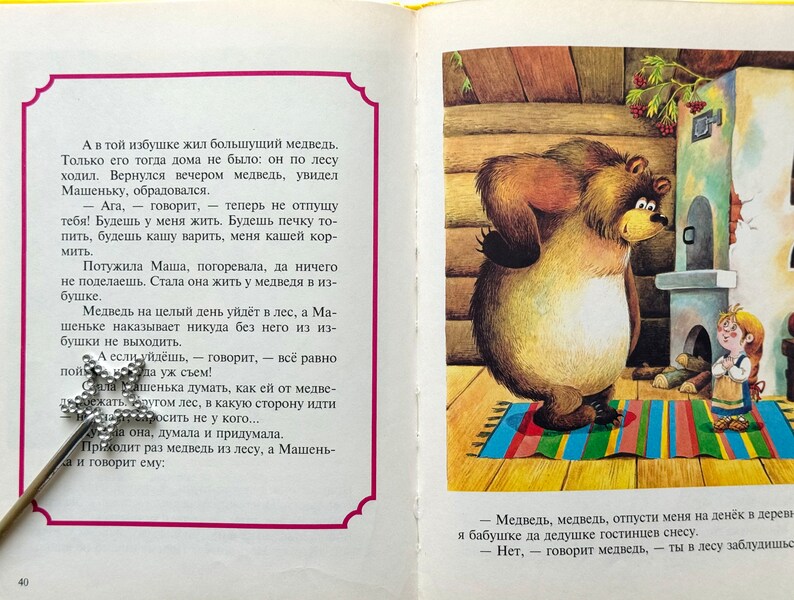 May include: A brown bear stands in a wooden cabin with a small girl. The bear is looking at the girl, who is holding a small wooden spoon. The cabin has a brick fireplace and a wooden door. The text in the image reads: "Aga, -  говорит, -  теперь не отпущу тебя! Будешь у меня жить. Будешь печку то-пить, будешь кашу варить, меня кашей кор-мить."