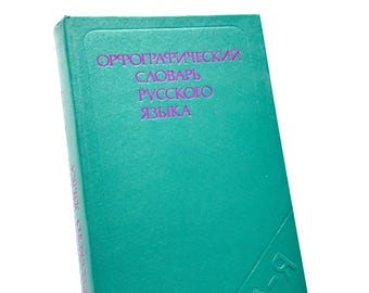 May include: A teal-colored book with the title "Orthographic Dictionary of the Russian Language" in purple lettering. The book's spine also features text in Russian. The book is set against a white background.