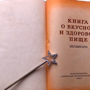 May include: A vintage book titled "Книга о вкусной и здоровой пище" (Book of Delicious and Healthy Food) with a silver star-shaped bookmark. The book was published in 1964 by "Пищевая промышленность" (Food Industry).