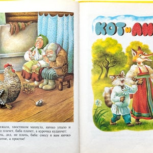 May include: A children's book illustration featuring a fox and a cat in a forest setting. The fox is wearing a red and blue dress and holding a bouquet of white flowers. The cat is wearing a blue shirt and white pants and holding a single white flower. The book title "KOT ANGA" is written in large, colorful letters at the top of the page.