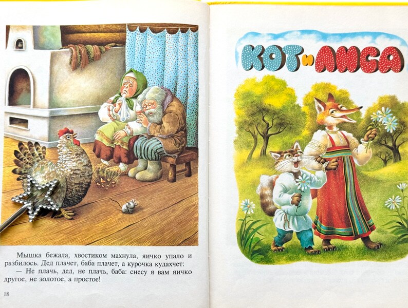 May include: A children's book illustration featuring a fox and a cat in a forest setting. The fox is wearing a red and blue dress and holding a bouquet of white flowers. The cat is wearing a blue shirt and white pants and holding a single white flower. The book title "KOT ANGA" is written in large, colorful letters at the top of the page.