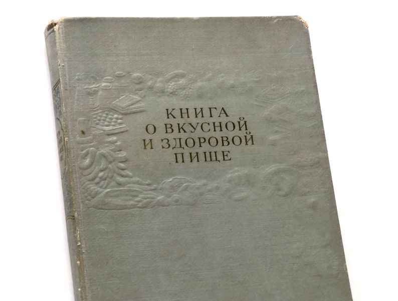 May include: A vintage book with a light blue cover and embossed details. The title reads "Книга о вкусной и здоровой пище" which translates to "Book about tasty and healthy food".