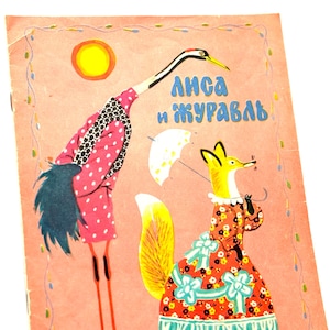 Pode incluir: Capa de livro infantil vintage com fundo rosa e ilustrações de um grou e uma raposa. O grou usa um casaco rosa com bolinhas, e a raposa está em um vestido floral. O texto "Лиса и журавль" está em azul.