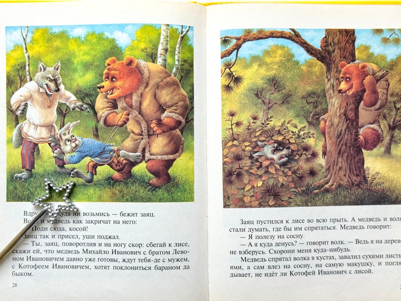 May include: An illustrated book page featuring a scene with a wolf, a bear, and a rabbit. The wolf is wearing a blue and white patterned shirt and a red sash. The bear is wearing a brown coat. The rabbit is wearing a blue shirt and a red sash. The text on the page reads: "Вдруг... куда ни возьмись - бежит заяц. Вот и медведь как закричат на него: Поди сюда, косой!"