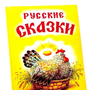May include: A yellow book cover with the title "Русские сказки" in red letters. The cover features an illustration of a hen sitting in a basket with a golden egg.