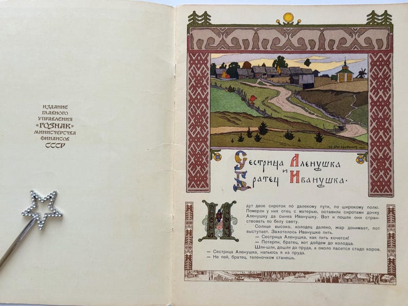 May include: An open book with a colorful illustration of a rural landscape, featuring a winding road, buildings, and a church. The text in Russian reads "Sister Alyonushka and Brother Ivanushka."