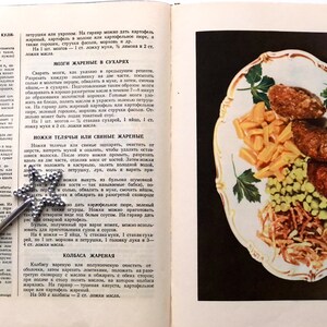 May include: A vintage cookbook open to a page with a recipe for fried brains. The recipe is written in Russian. The page also includes a photo of a plate of fried brains with peas, french fries, and parsley.