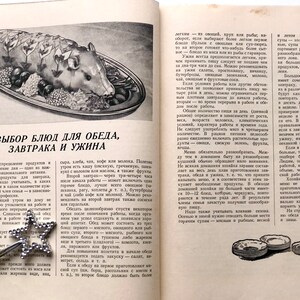 May include: A vintage cookbook open to a page titled "Choice of Dishes for Lunch, Breakfast and Dinner". The page features a black and white illustration of a roasted pig with vegetables and herbs on a silver platter.