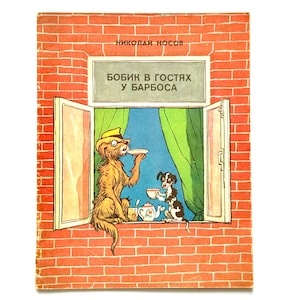 Puede incluir: Portada de libro infantil vintage con una ilustración de dos perros en una ventana. El título, "Bobik in Gostyakh u Barbosa", está en un rectángulo blanco. Un perro lleva sombrero y sirve un plato.