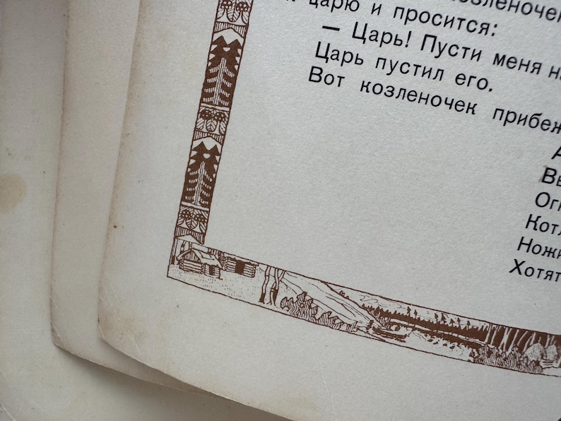 May include: Close-up of a vintage book page with text in a foreign language. The page has a decorative brown border featuring trees, a cabin, and a landscape scene. The paper is aged with a slightly yellowed tone.