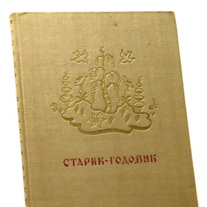 Könnte beinhalten: Ein tannenes Buch mit einem goldgeprägten Design eines Baumes und Vögeln auf dem vorderen Umschlag. Der Titel "Старик-Годовик" ist in roten Buchstaben unter dem Design gedruckt.