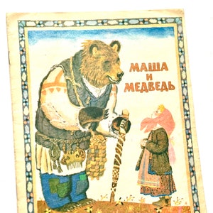 Pode incluir: Uma capa de livro infantil vintage com um urso marrom vestindo uma camisa azul e segurando um cajado. Uma menina com um vestido vermelho e marrom está à direita do urso. O título do livro é "Маша и Медведь" em russo.