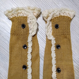 May include: A pair of brown knitted leg warmers with white crocheted trim and black buttons.
