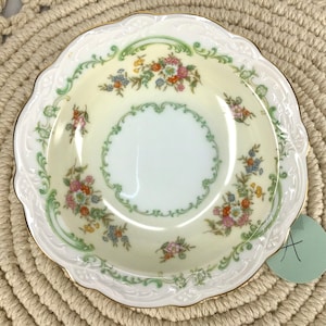 May include: A small, white porcelain bowl with a scalloped edge and a gold rim. The bowl is decorated with a floral pattern in shades of green, pink, and blue.