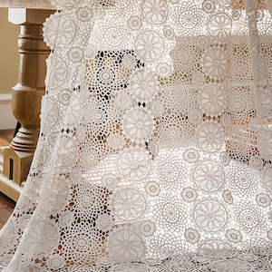 May include: White crochet table runner with a delicate floral pattern. The runner is made of a lightweight, airy fabric and features a circular design.