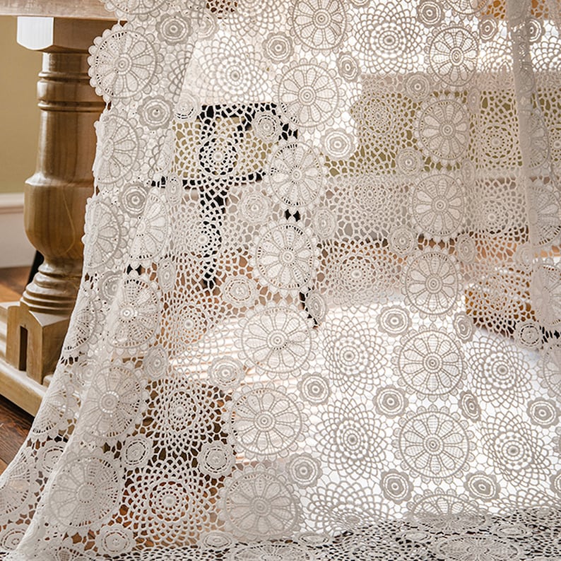 May include: White crochet table runner with a delicate floral pattern. The runner is made of a lightweight, airy fabric and features a circular design.
