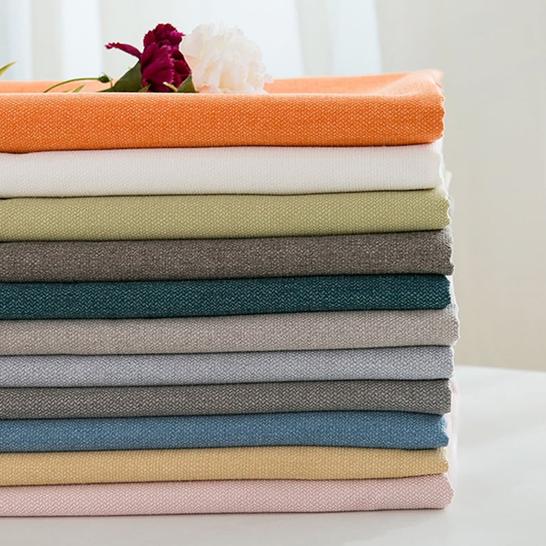May include: A stack of 12 fabric swatches in various colors, including orange, white, green, brown, teal, gray, blue, yellow, and pink. The fabric has a subtle texture.