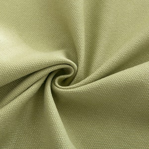 May include: Close-up of a light green fabric with a textured surface. The fabric is folded and draped, showing its soft and smooth texture.