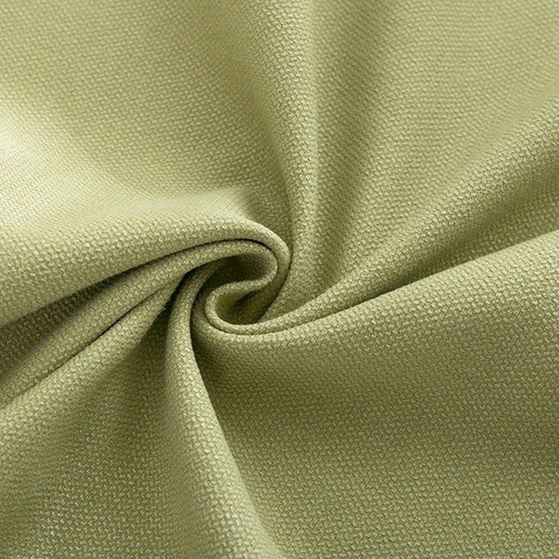May include: Close-up of a light green fabric with a textured surface. The fabric is folded and draped, showing its soft and smooth texture.