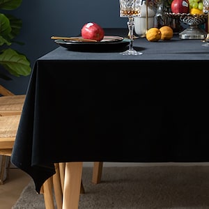May include: A black velvet tablecloth draped over a wooden table with a red apple on a plate and two lemons on the table.