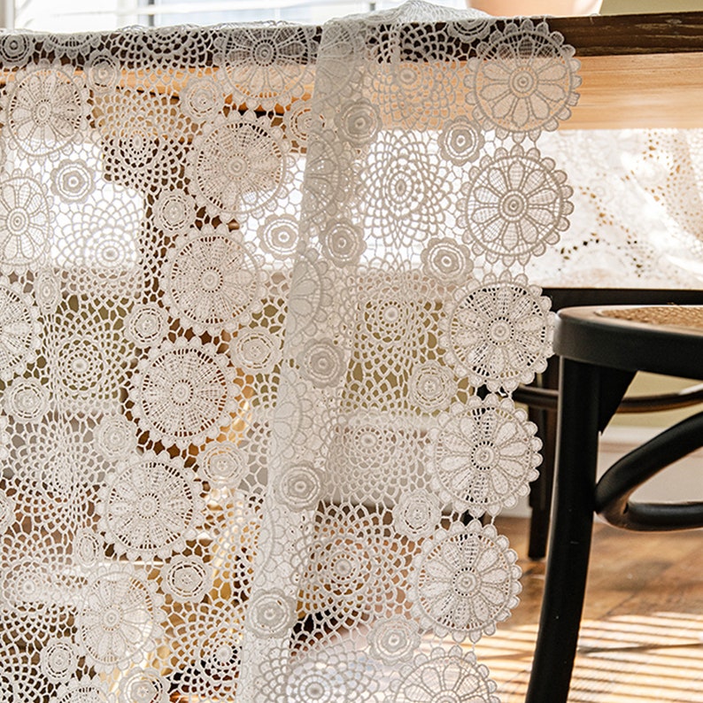 May include: White crochet table runner with a delicate floral pattern. The runner is made of a lightweight, airy fabric and features a scalloped edge.