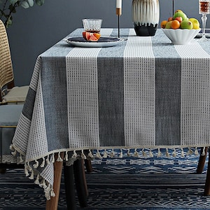 Puede incluir: Un mantel de mesa a rayas grises y blancas con un borde de flecos. El mantel está hecho de un tejido suave y tejido y tiene un sutil patrón de puntos.