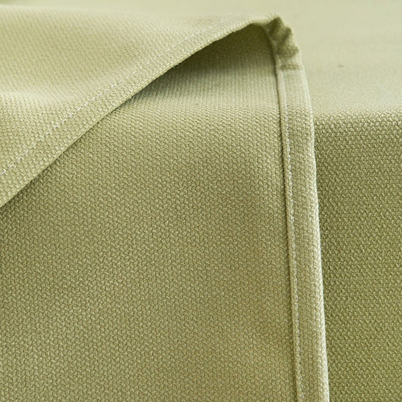 May include: Close-up of a light green fabric with a subtle textured pattern. The fabric has a seam running down the side.