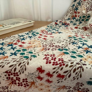 May include: A white tablecloth with a floral pattern featuring red, blue, and green flowers. The tablecloth has a subtle texture and a slightly off-white background.