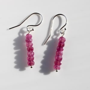 May include: A pair of silver earrings with pink gemstone beads. Each earring has a silver hook and a small silver bead at the bottom.