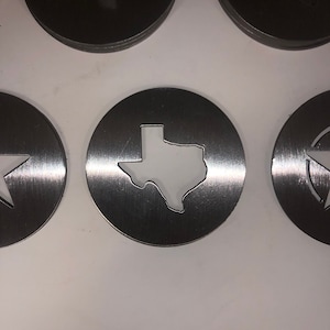 Könnte beinhalten: Satz mit sechs Untersetzern aus silbernem Metall mit einem ausgeschnittenen Design des Bundesstaates Texas. Die Untersetzer haben eine gebürstete Oberfläche.