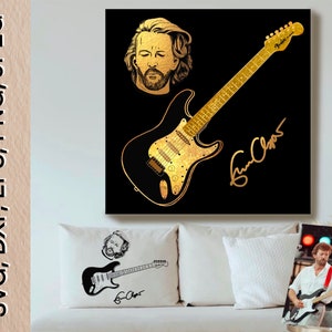 May include: A black and gold digital art print featuring a portrait of Eric Clapton with a gold Fender Stratocaster guitar and his signature. The print is on a black background.