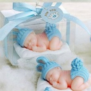 May include: Two blue and white baby figurines in a clear plastic box with a blue ribbon. The figurines are sleeping and wearing blue and white knitted hats and outfits. The box has a tag that says "For You".