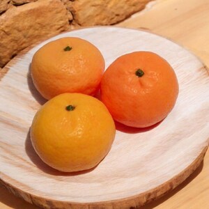 Pode incluir: Três laranjas inteiras em um prato de madeira claro. As laranjas são de cor laranja brilhante e têm uma textura lisa.