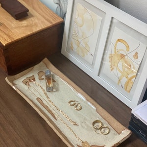 Könnte beinhalten: Ein rechteckiges Keramiktablett mit weißem Überzug und braunen Akzenten. Das Tablett ist gefüllt mit goldfarbenem Schmuck, darunter eine Halskette, Ohrringe und Ringe. Das Tablett steht auf einer Holzoberfläche.