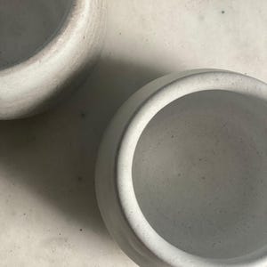 An overhead close-up shows the speckled off-white interiors of two ceramic cups on a light-colored surface.