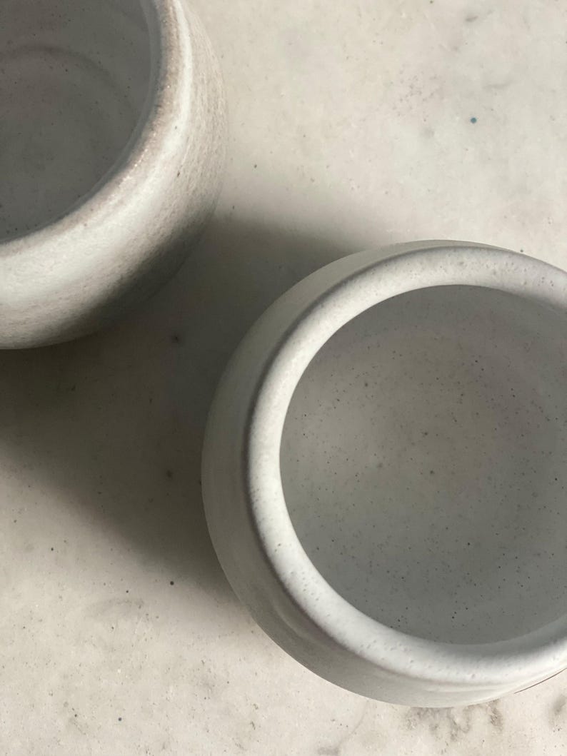 An overhead close-up shows the speckled off-white interiors of two ceramic cups on a light-colored surface.