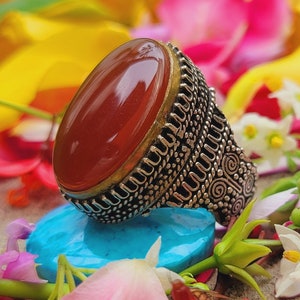 May include: A silver ring with an oval-shaped carnelian gemstone. The ring has intricate details and a textured band.