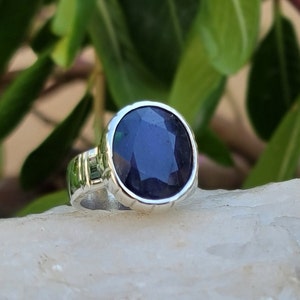May include: A silver ring with a dark blue gemstone. The ring has a textured band and a round bezel setting.