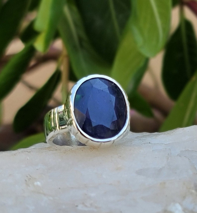 May include: A silver ring with a dark blue gemstone. The ring has a textured band and a round bezel setting.