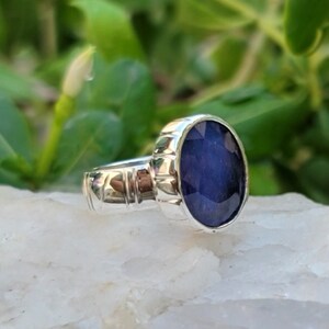 May include: A silver ring with a dark blue oval gemstone. The ring has a textured band.