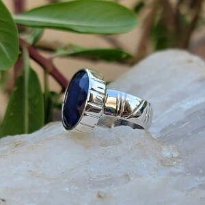 May include: A silver ring with a deep blue oval gemstone set in a textured band.